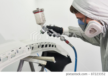 Mechanic painting bumper of a car with sprayer in painting booth in repair auto service 87223352