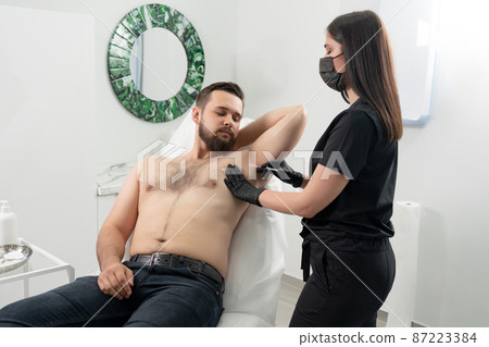 Doctor doing injection from hyperhidrosis. Man receiving an underarm treatment in cosmetology clinic Doctor doing injection from hyperhidrosis. Man receiving an underarm treatment in cosmetology clinic 87223384