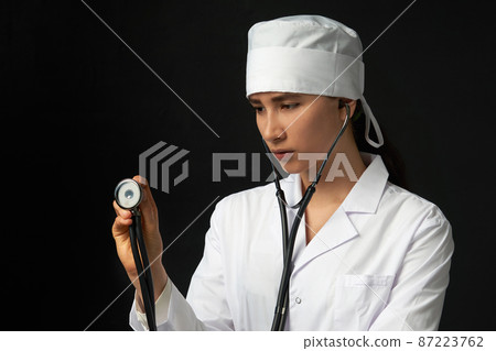 Cropped view of young female doctor holding stethoscope hanging on her neck, studio shot over black background with copy space 87223762