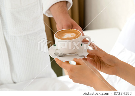 Closeup of a man bringing coffee to his girlfriend lying in bed Closeup of a man bringing coffee to his girlfriend lying in bed 87224193