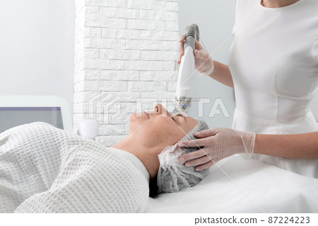 Mature woman receiving laser treatment in cosmetology clinic Mature woman receiving laser treatment in cosmetology clinic 87224223