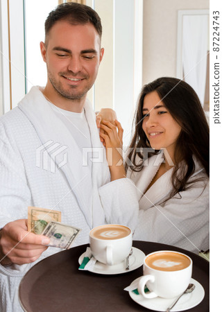 Room service delivering coffee to a hotel room for married couple wearing bathrobe who is giving dollar tips 87224743