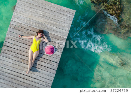 Aerial view of woman laying on wooden pier at sunny summer day in Cancun, Mexico, top view. Young sexy woman wearing bright swimsuit in summertime in Caribbean. Summer beach vacation concept Aerial view of woman laying on wooden pier at sunny summer day in Cancun, Mexico, top view. Young sexy woman wearing bright swimsuit in summertime in Caribbean. Summer beach vacation concept 87224759