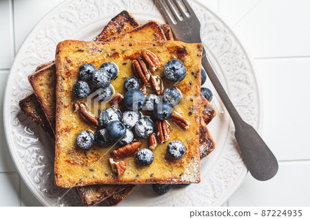 French toast with blueberries, pecan and maple syrup for breakfast on white plate. French toast with blueberries, pecan and maple syrup for breakfast on white plate. 87224935