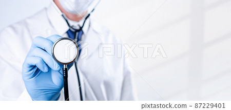 Stethoscope doctor medical background. Happy nurse in hospital uniform, blue gloves holding stethoscope isolated on white. Medicine service and healthcare concept. 87229401