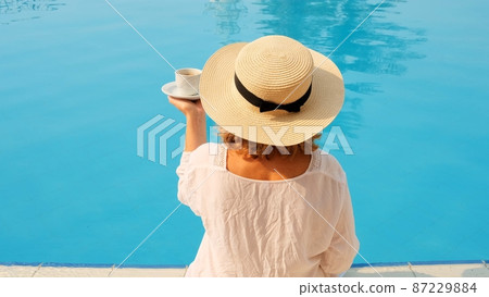 The culture of drinking tea and coffee. Woman with straw hat drinking hot drink from a cup near blue The culture of drinking tea and coffee. Woman with straw hat drinking hot drink from a cup near blue 87229884