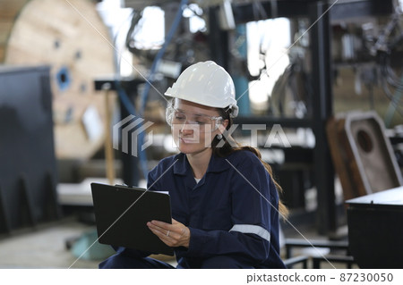 Female industrial worker working with manufacturing equipment in a factory 87230050