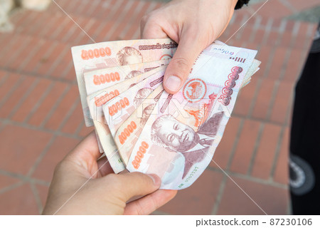 Cropped shot view of someone giving or payment banknotes of Laos kip money to other person. Kip is the national currency of Laos. Cropped shot view of someone giving or payment banknotes of Laos kip money to other person. Kip is the national currency of Laos. 87230106
