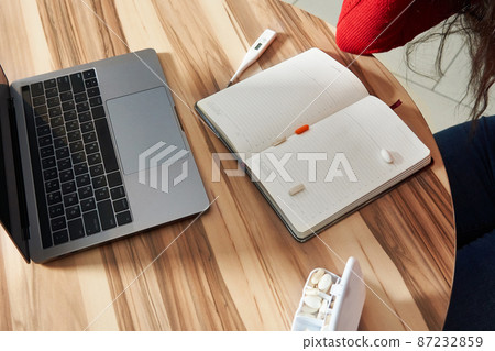 sick woman with pills and thermometer on a table working on a laptop from home on quarantine isolation. sick woman with pills and thermometer on a table working on a laptop from home on quarantine isolation. 87232859