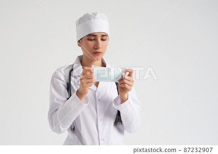 Portrait of young female doctor putting on protective medical face mask on white background, copy space Portrait of young female doctor putting on protective medical face mask on white background, copy space 87232907