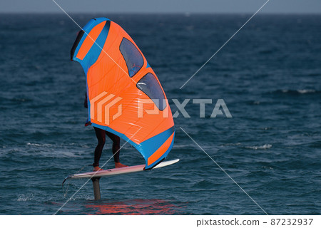 A man is wing foiling using handheld inflatable wings and hydrofoil surfboards in a blue ocean, rider on a wind wing board, surf the waves 87232937
