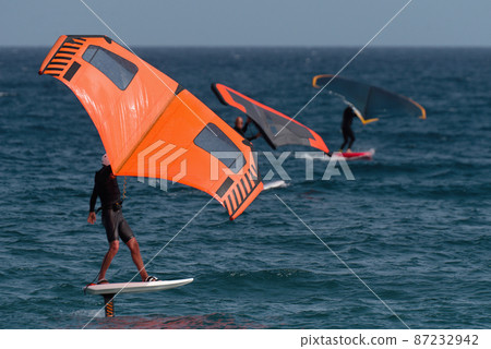A group is wing foiling using handheld inflatable wings and hydrofoil surfboards in a blue ocean, rider on a wind wing board, surf the waves A group is wing foiling using handheld inflatable wings and hydrofoil surfboards in a blue ocean, rider on a wind wing board, surf the waves 87232942