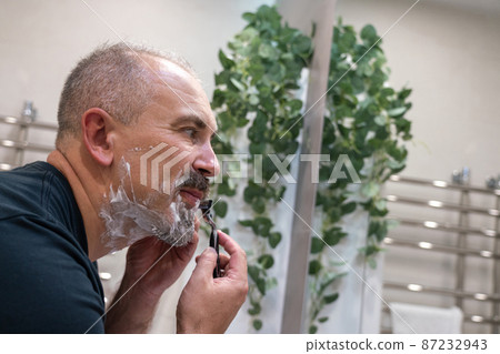 Middle aged handsome man shaving his beard in bathroom 87232943