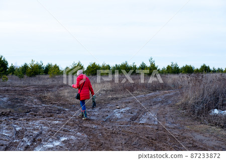 A refugee woman walks along a broken and dirty road against the background of a forest. A lonely woman goes into the forest. A refugee woman walks along a broken and dirty road against the background of a forest. A lonely woman goes into the forest. 87233872