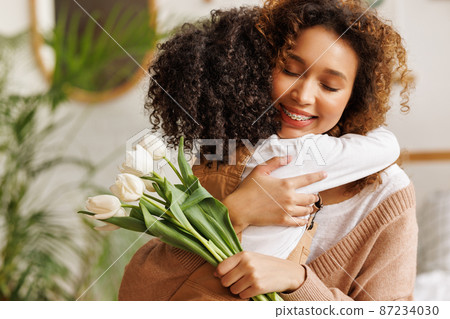 Young ethnic woman mother with flower bouquet embracing son while getting congratulations on Mother's day Young ethnic woman mother with flower bouquet embracing son while getting congratulations on Mother's day 87234030