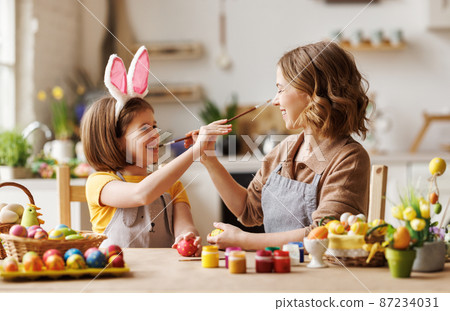 Joyful happy family mom and daughter having fun and fooling around while decorating Easter eggs Joyful happy family mom and daughter having fun and fooling around while decorating Easter eggs 87234031