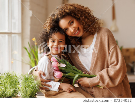 Young ethnic woman mother with flower bouquet embracing son while getting congratulations on Mother's day Young ethnic woman mother with flower bouquet embracing son while getting congratulations on Mother's day 87234032