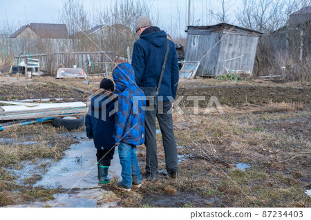 Dad and two children look at the destroyed area. Village after the flood. Refugees in a destroyed village. 87234403