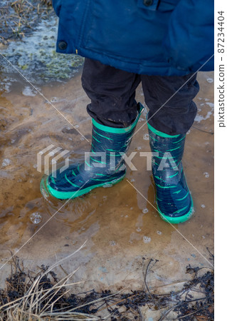 A child in boots walks and jumps in a muddy puddle after rain. Mud after melting snow. 87234404