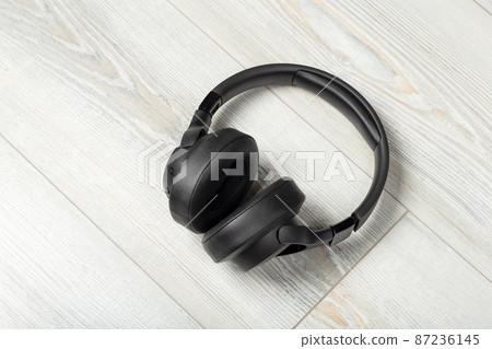 Wireless headphones on a white wooden laminate floor background. Soundproofing, music and sound in the room concept. Wireless headphones on a white wooden laminate floor background. Soundproofing, music and sound in the room concept. 87236145