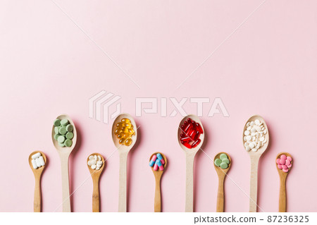 Top view Variety of vitamin and mineral pills in wooden spoon on Colored background. Top view of assorted pharmaceutical medicine pills. Dietary supplement healthcare product 87236325