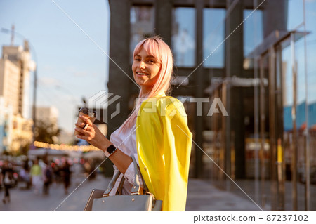 Joyful woman standing on the street and holding cup of coffee Joyful woman standing on the street and holding cup of coffee 87237102