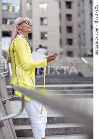 Woman with smartphone looking at sky from public staircase Woman with smartphone looking at sky from public staircase 87237105