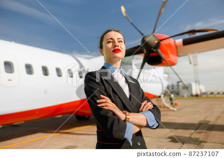 Female airline worker standing near plane at airport Female airline worker standing near plane at airport 87237107