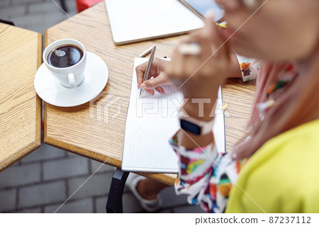 Person writing with steel pen in notepad near coffee cup Person writing with steel pen in notepad near coffee cup 87237112