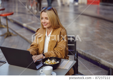 Young lady dressed in trench coat sitting at table in street cafe Young lady dressed in trench coat sitting at table in street cafe 87237222