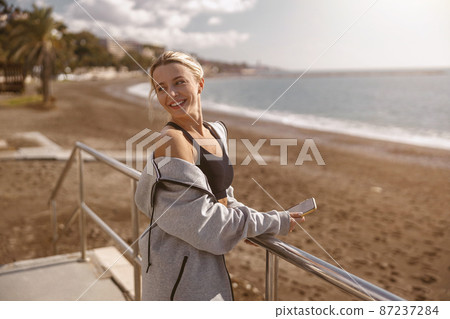 Smiling sporty woman using smartphone on beach Smiling sporty woman using smartphone on beach 87237284