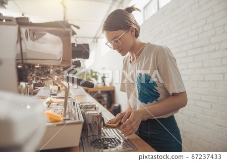 Charming female barista cleaning counter in coffee shop 87237433