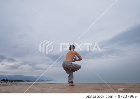 Caucasian man with naked torso practicing wushu on the seashore. Caucasian man with naked torso practicing wushu on the seashore. 87237969