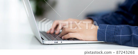 Employee young man typing and working on laptop computer on desk at home. 87243268