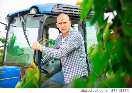 Skilled male farmer working on farm tractor in orchard 87243373