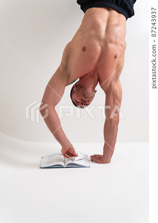 Bodybuilder reads the book on a white background isolated at the bottom of his head on his hands male book macho, white guy shirtless, intellectual standing. ABS beach tan Bodybuilder reads the book on a white background isolated at the bottom of his head on his hands male book macho, white guy shirtless, intellectual standing. ABS beach tan 87243937