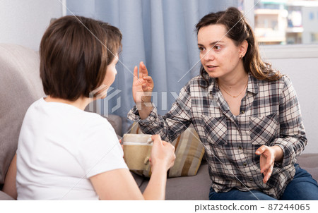 Smiling young female friends gossiping on sofa in home interior Smiling young female friends gossiping on sofa in home interior 87244065