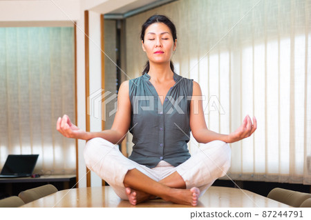 Businesswoman sitting at the table in lotus position Businesswoman sitting at the table in lotus position 87244791