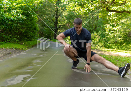 A young enduring athletic athlete is doing stretching in the forest outdoors, around the forest, oak trees.run runner nature, fitness jogger athletic person jog, woods man. Autumn running, feet 87245139