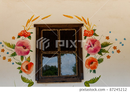 Clay wall of a traditional Ukrainian village house painted with bright floral patterns around the old window 87245212