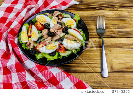 Tasty tuna salad with lettuce, black olives, eggs and fresh vegetables on wooden table 87245295