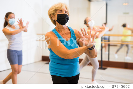 Active mature woman in a protective mask practices energetic swing in the studio Active mature woman in a protective mask practices energetic swing in the studio 87245602