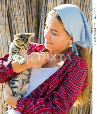 Smiling young female farmer holding tabby kitten in hands 87245608