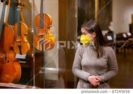 Female museum visitor in mask examining ancient musical instruments Female museum visitor in mask examining ancient musical instruments 87245656