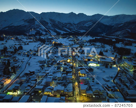 Snow-covered dusk Hakuba mountain range and Hakuba village cityscape Hakuba village, Nagano prefecture (aerial view by drone) 87245703