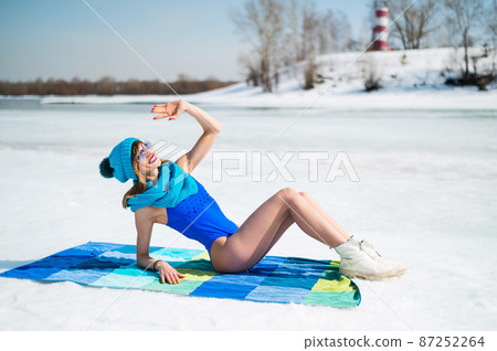 Beautiful caucasian woman in a swimsuit and a hat sunbathes on the snow. Beautiful caucasian woman in a swimsuit and a hat sunbathes on the snow. 87252264
