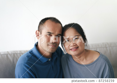 Portrait of Asian mature couple sitting in the living room. wife and husband hugging, holding hand with happiness and cheerful. Love, safety, and insurance family concept. Portrait of Asian mature couple sitting in the living room. wife and husband hugging, holding hand with happiness and cheerful. Love, safety, and insurance family concept. 87258159