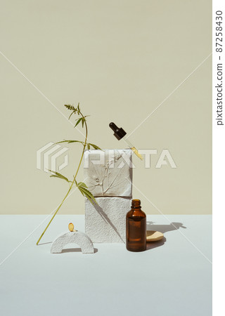 CBD oil in pipette and an open bottle on podium with a leaf of marijuana, hemp 87258430