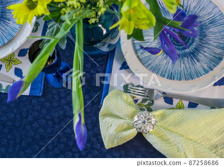 Table setting in blue and yellow colors. On a dark tablecloth a plate, a vase of flowers and decor Table setting in blue and yellow colors. On a dark tablecloth a plate, a vase of flowers and decor 87258686