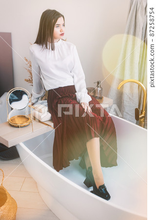 Portrait of fashionable women in red skirt, white blouse and stylish beige high-heeled shoes with a chain buckle posing in a bed Portrait of fashionable women in red skirt, white blouse and stylish beige high-heeled shoes with a chain buckle posing in a bed 87258754